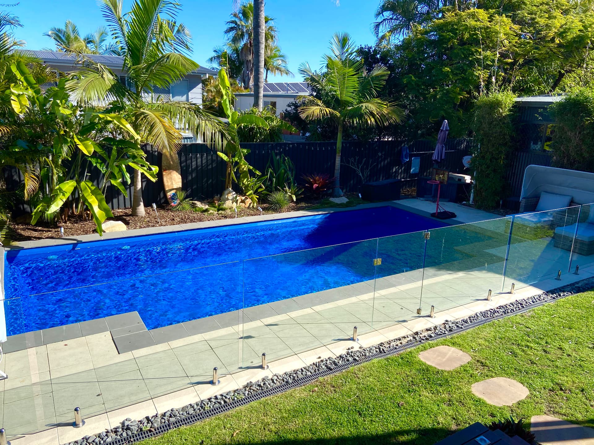 Pool with glass fencing, paved surround, lawn and established tropical planting
