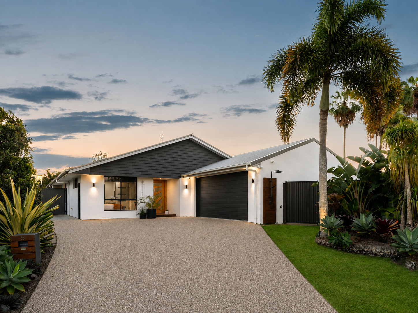 Front elevation at dusk with timber entry door, lighting and established planting