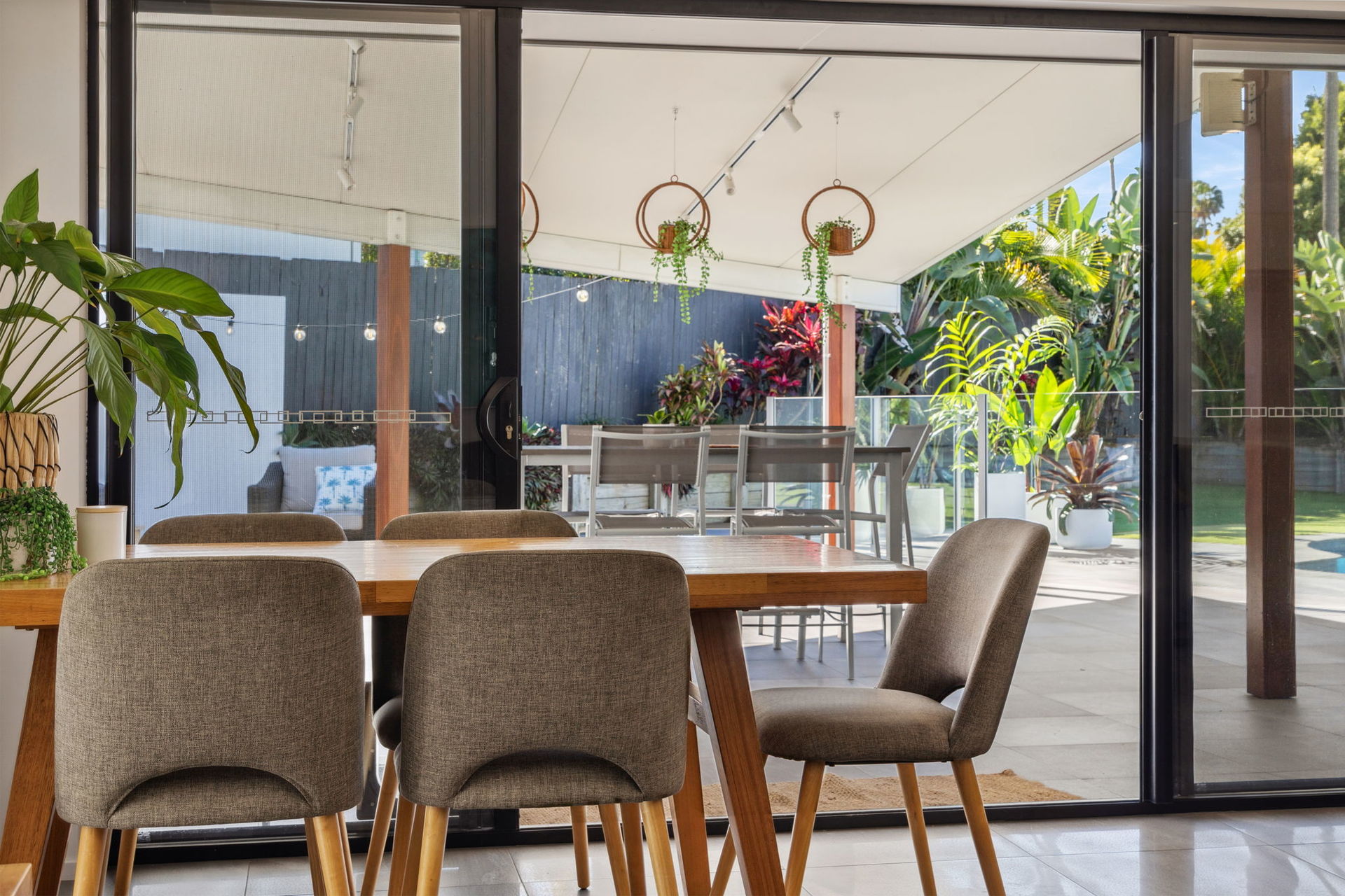 Dining table looking through wide sliding doors to a covered alfresco area and planting