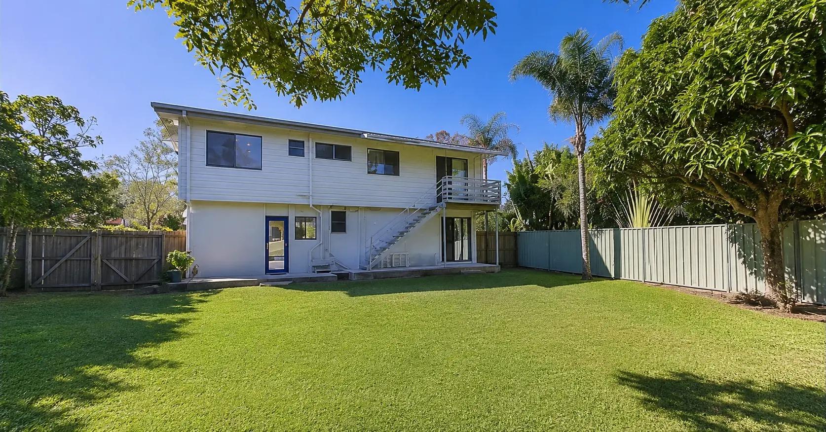 Original rear of the highset home with open lawn and a small upper landing