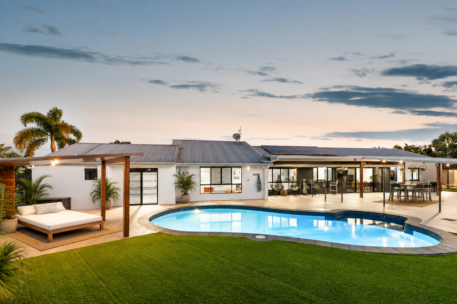 Rear elevation of the home at dusk with pool, lawn and covered outdoor entertaining area