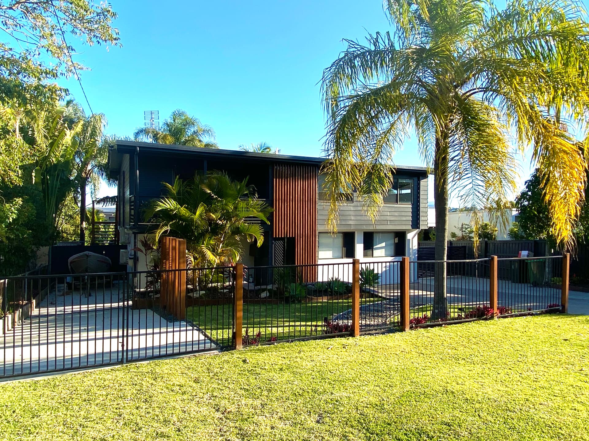 Renovated highset home facade with timber screening, dark cladding and tropical front garden