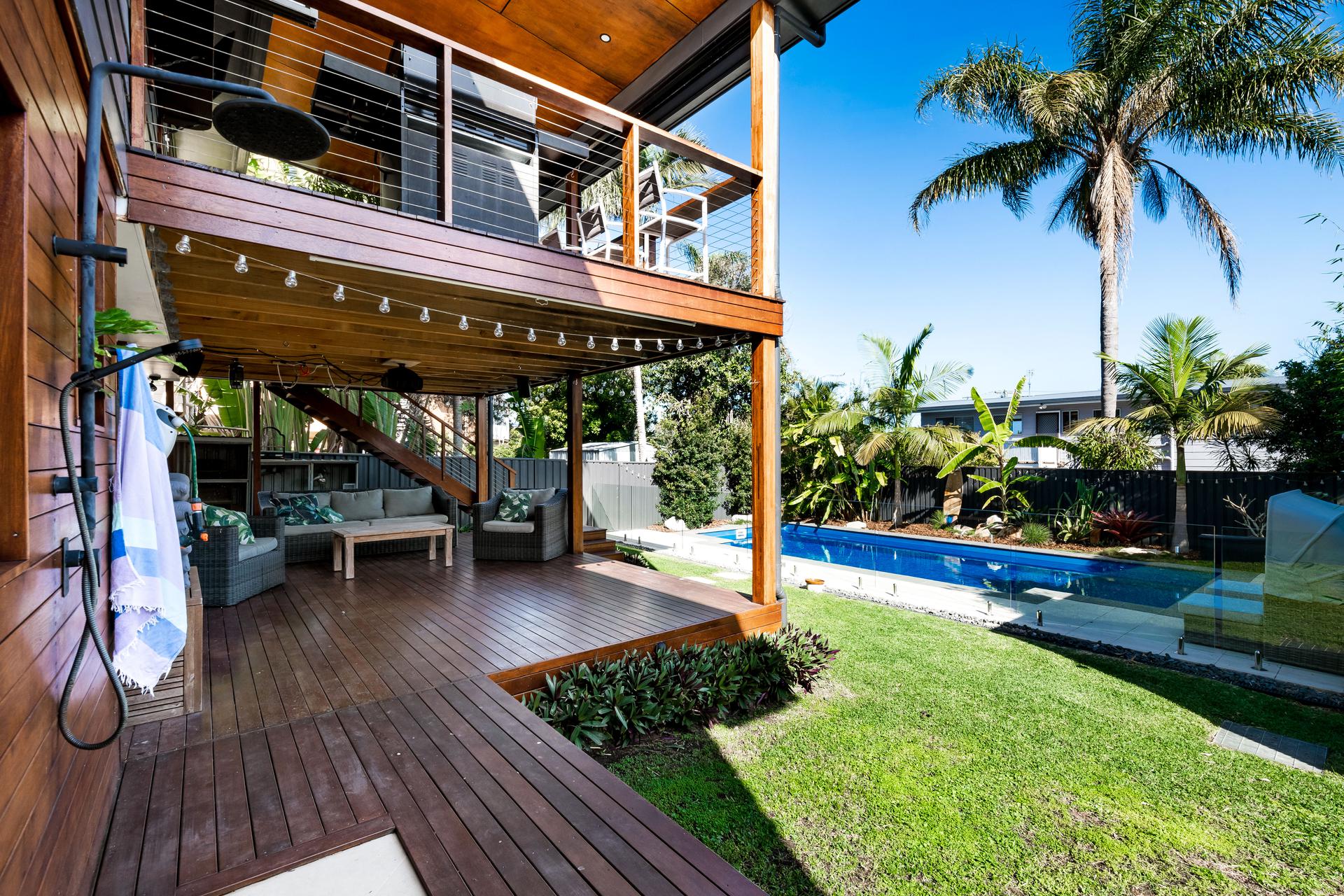Covered lower deck with lounge seating, outdoor shower and pool alongside